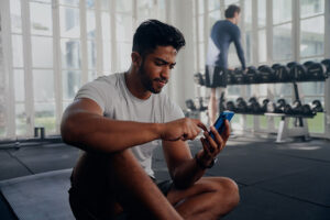 Pessoa na academia com o celular na mão, usando um app de treino com atenção e expressão confiante