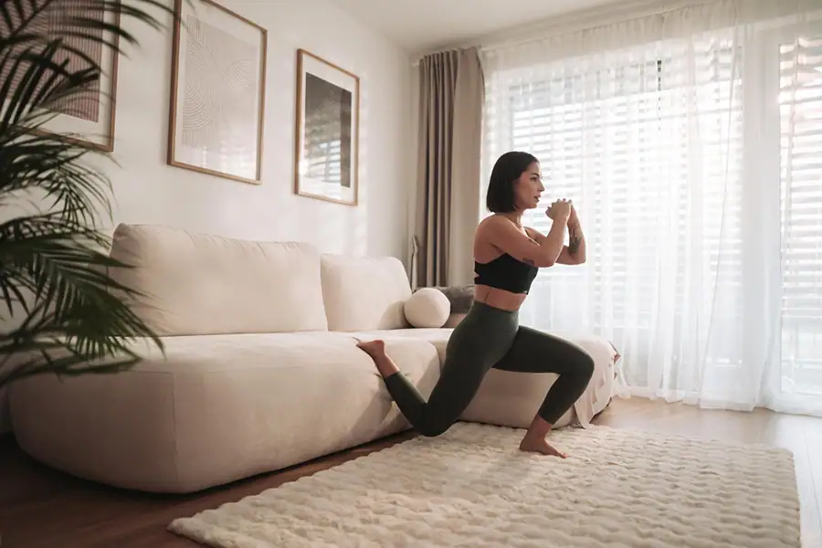 Mulher fazendo exercício de afundo na sala de casa.