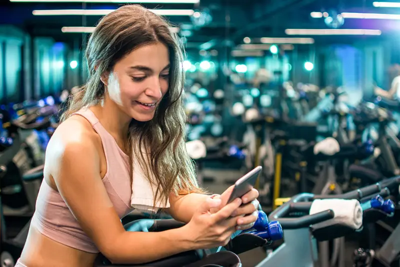 Aluno feliz utilizando um app de treino gratuito no celular durante a musculação