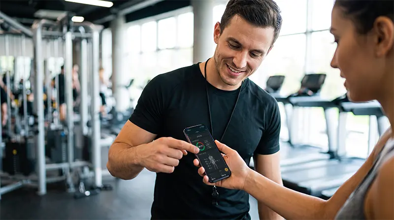 Personal trainer apontando para gráficos na tela de celular da aluna, mostrando na prática como fazer avaliação física online