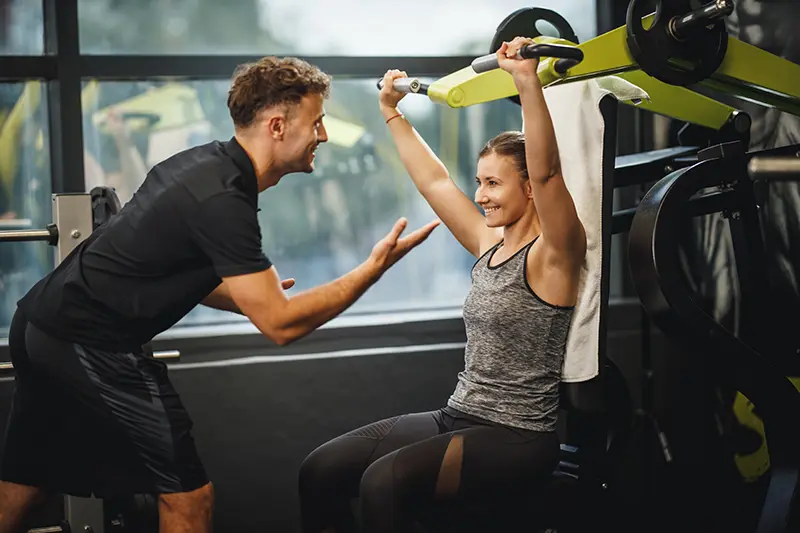 Personal trainer orientando uma aluna na academia, celebrando o dia dos professores
